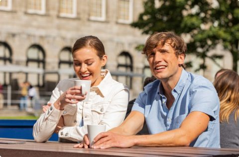 two people with cups of coffee smiling on a bench