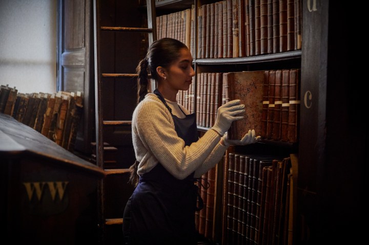 a woman putting a book back into a shelf in the old library