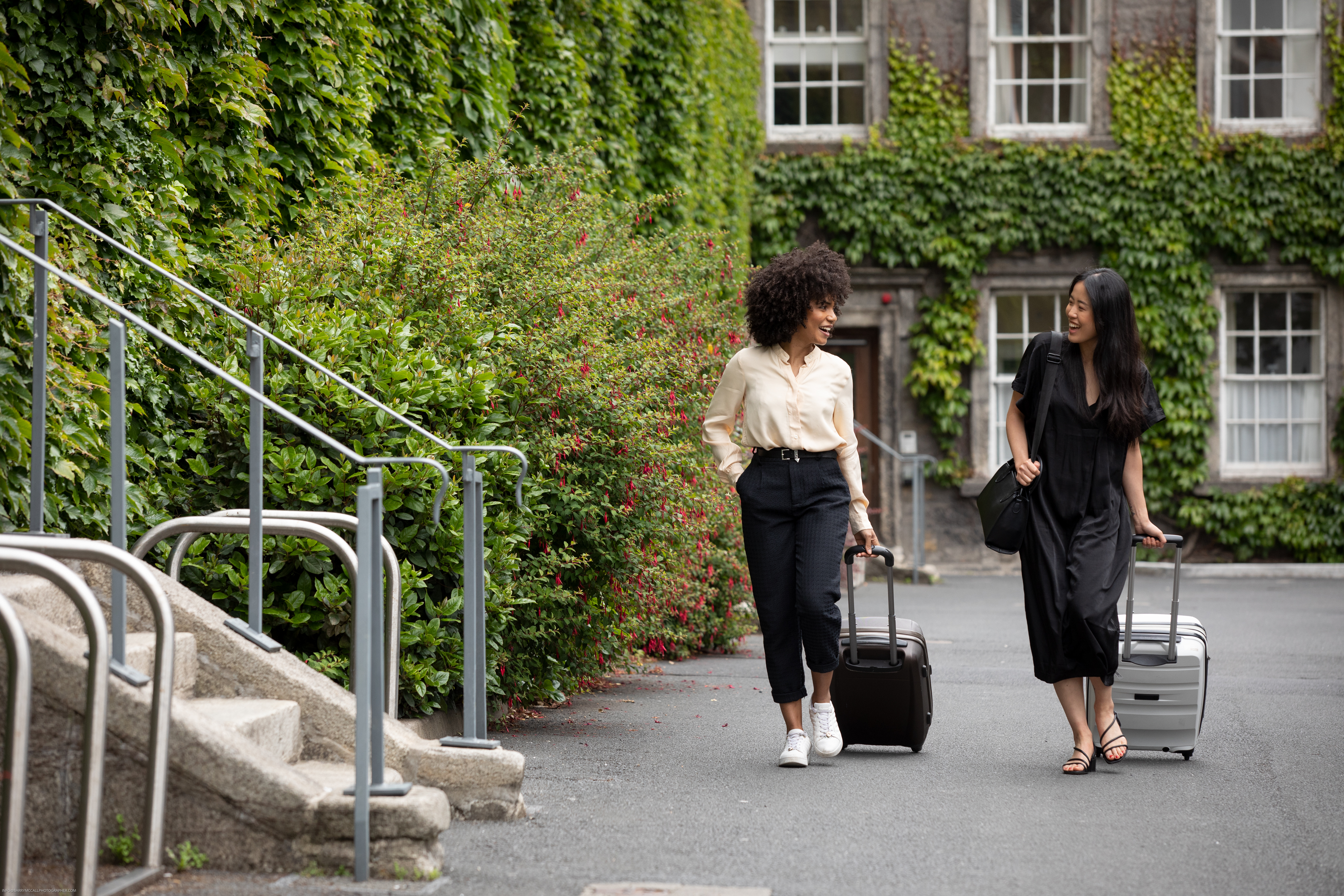 Two people walking on Trinity campus with suitcases