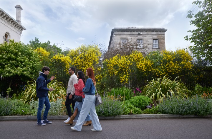 Three people and a tour guide walking along a path on the Trinity college campus