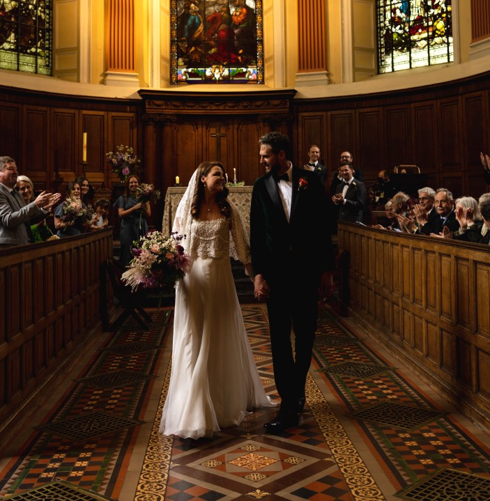 A bride and groom holding hands walking down the aisle at a chapel in Trinity College