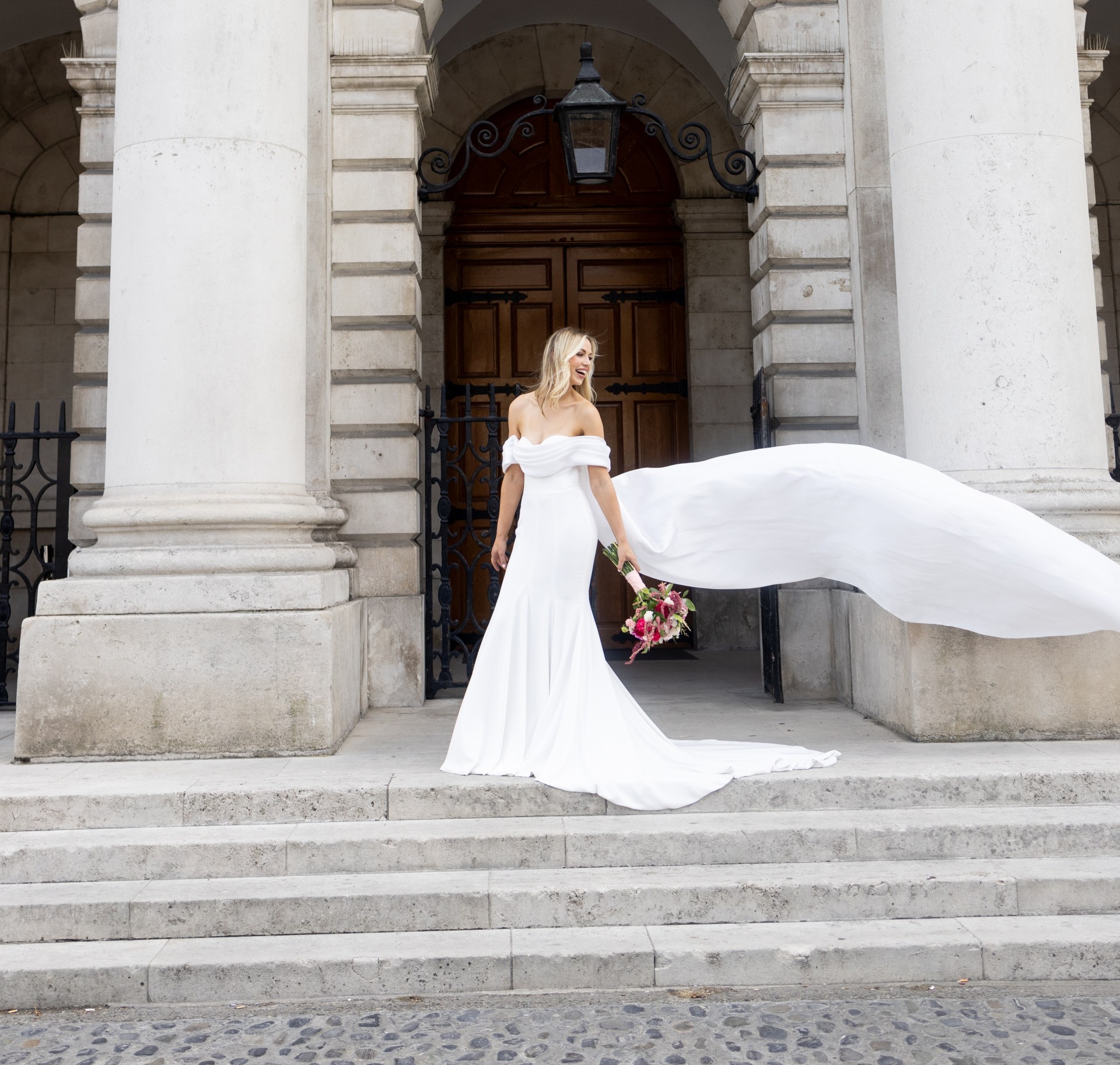 A bride in a white dress on the steps of an old building in Trinity college