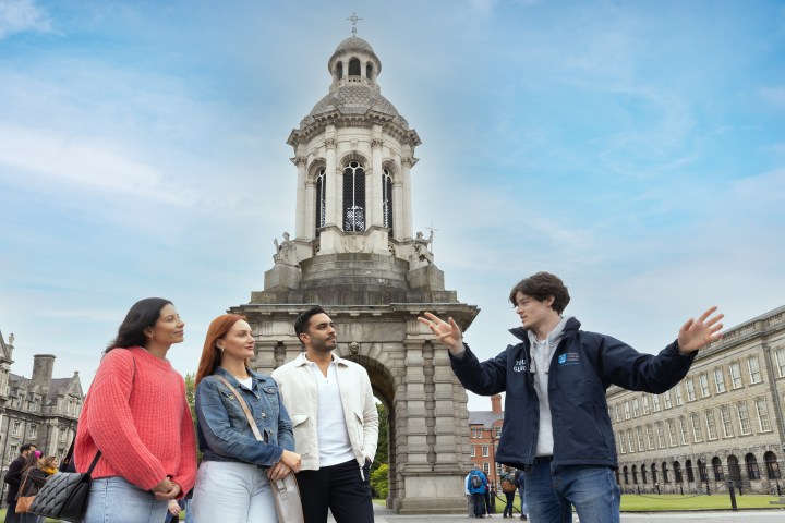 A tour guide with a group of three people in front of the bell tower of Front Square