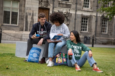 Three students wearing black, grey and green hoodies looking through Trinity College merchandise