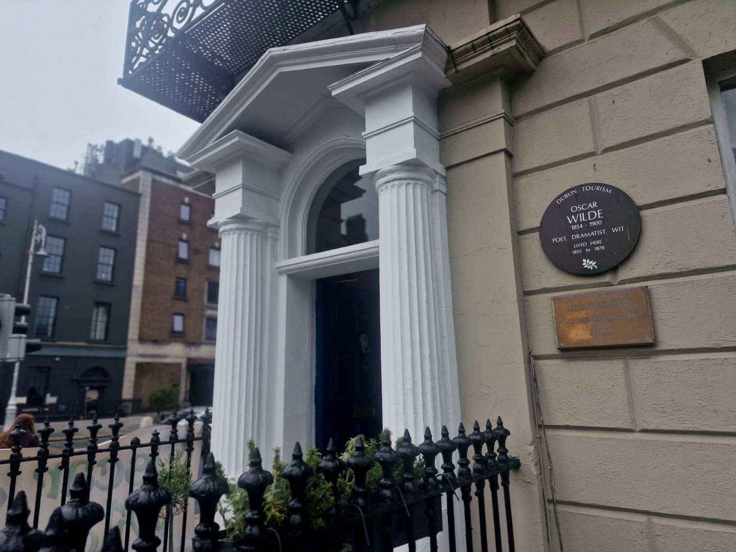 A corner building with white pillars and arch with an Oscar Wilde plaque on the wall