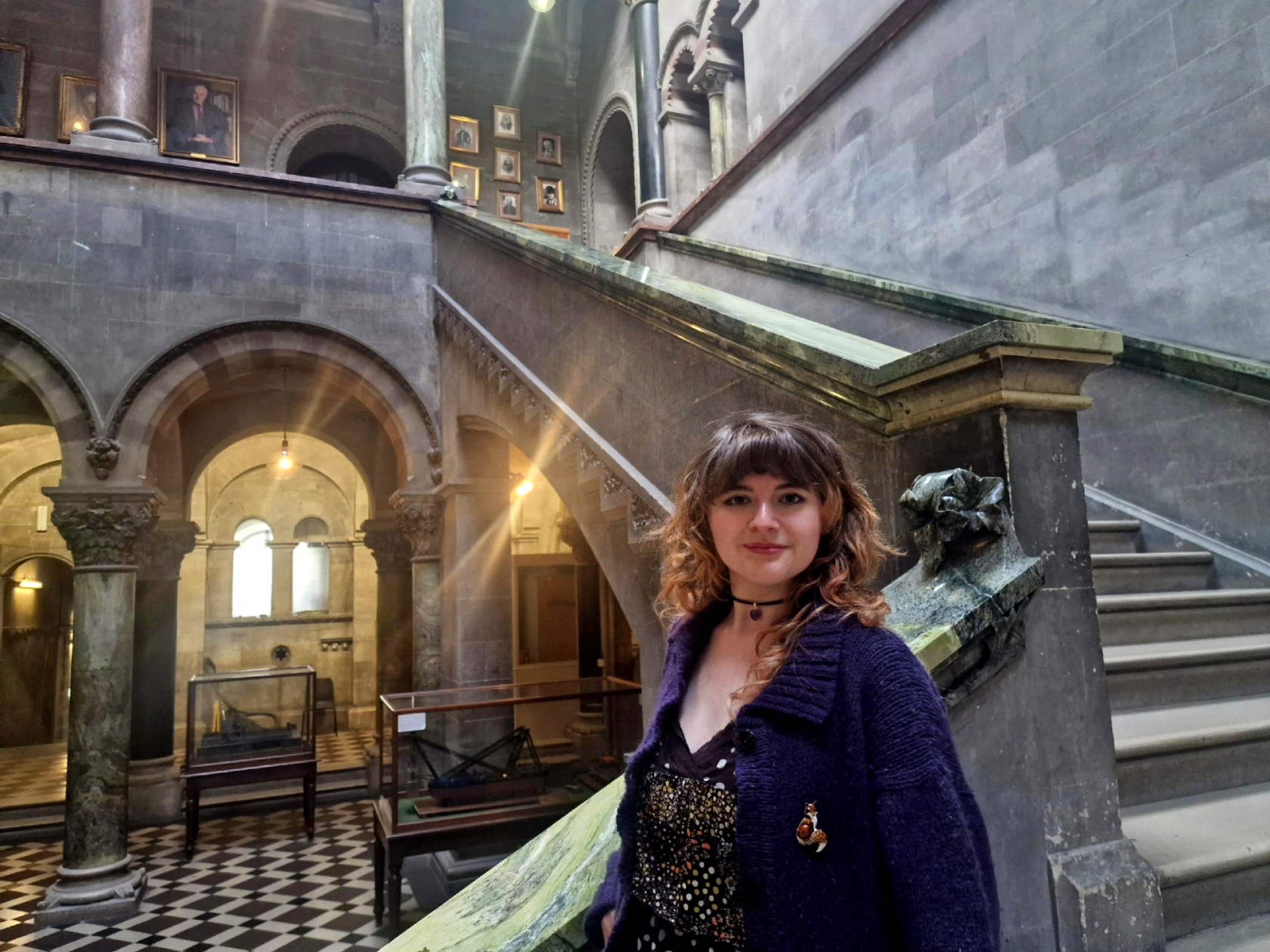 Author Genevieve Kilbride standing on the stairs of the Museum Building, wearing a navy cardigan and black jewelled t shirt