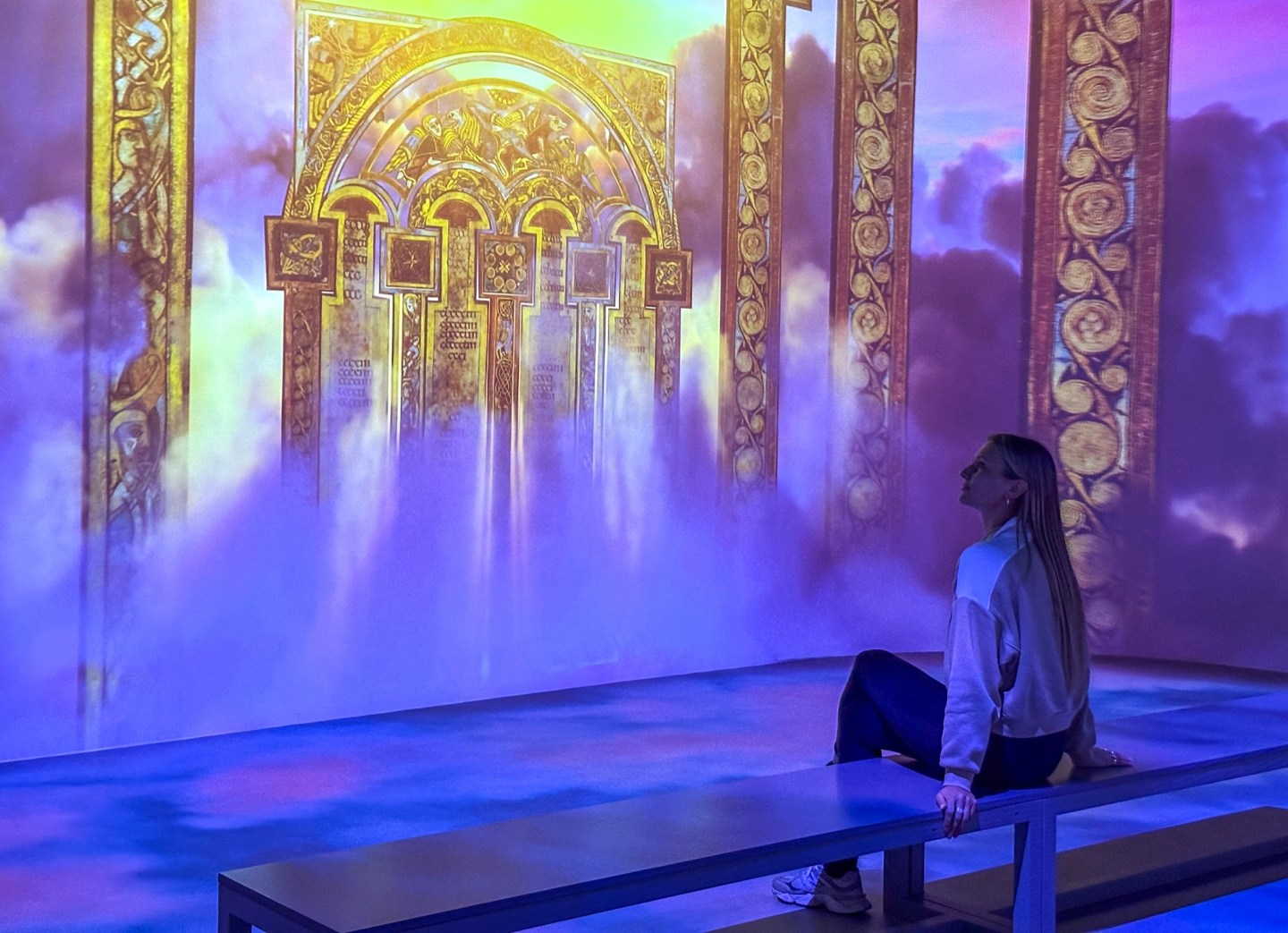 A woman sitting on a bench looking at the Book of Kells display