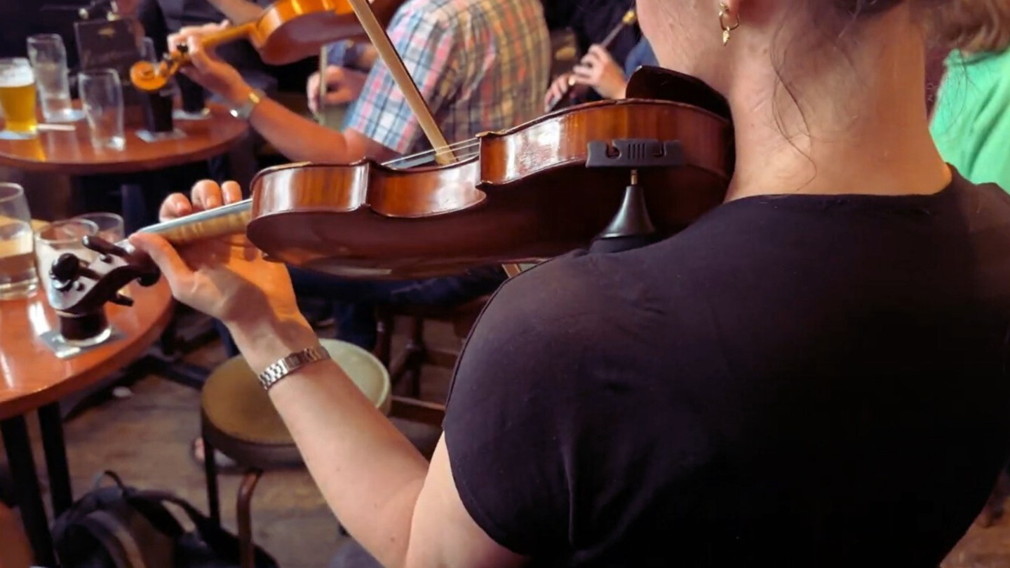 A woman plays the violin in a trad band in a pub