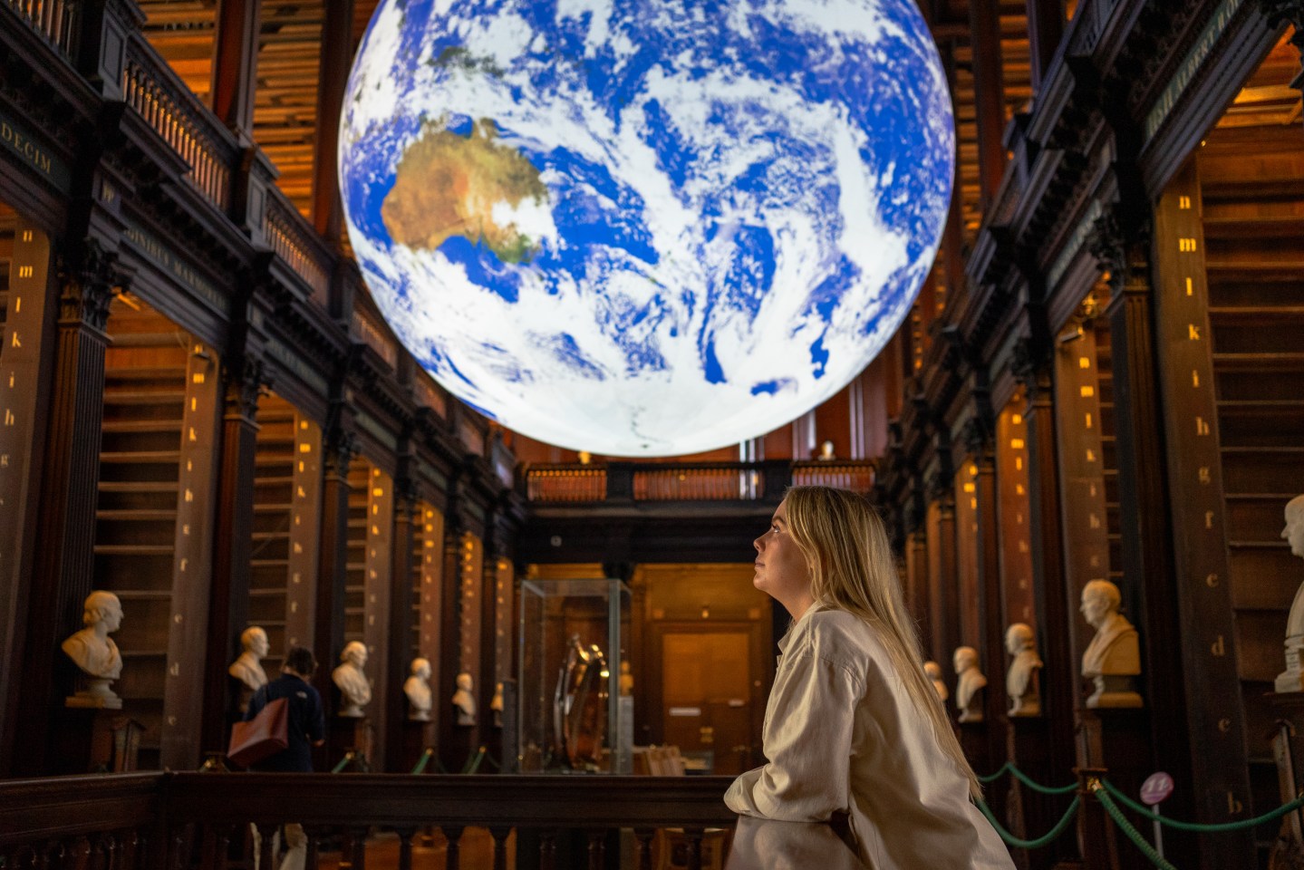 Image of a woman under the Gaia display, looking around the Long Room