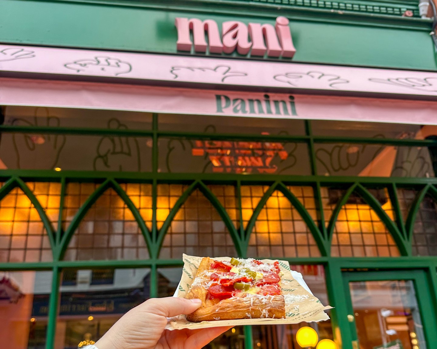 A hand holds out a pizza slice in front of Mani Pizza Dublin