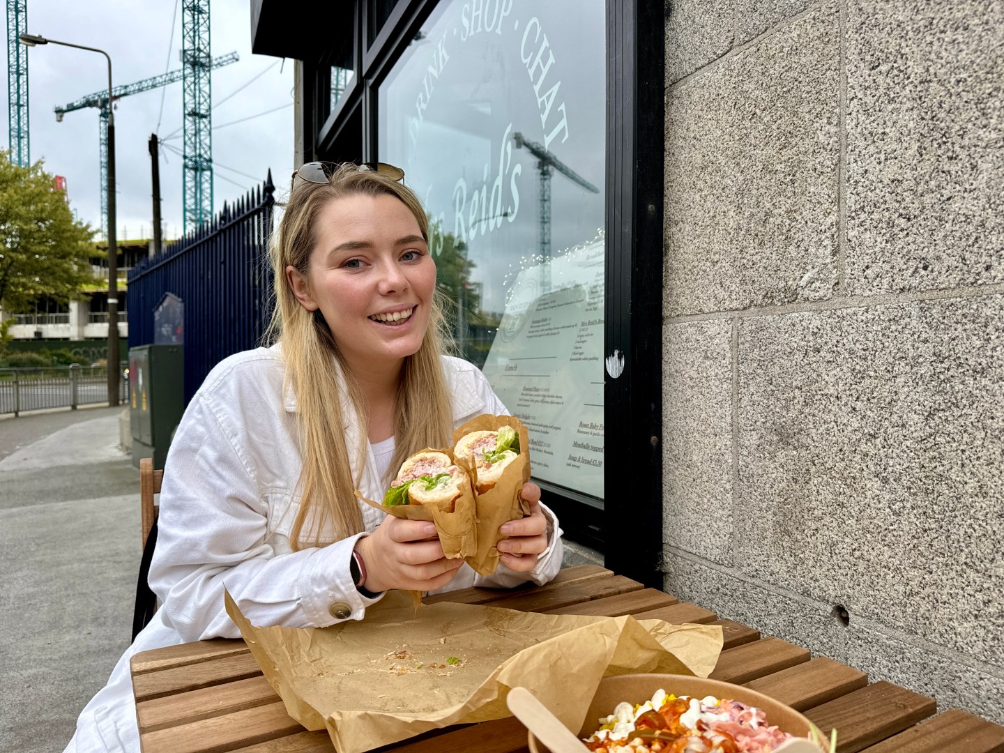 A woman sitting outside Mrs Reids, holding a sandwich