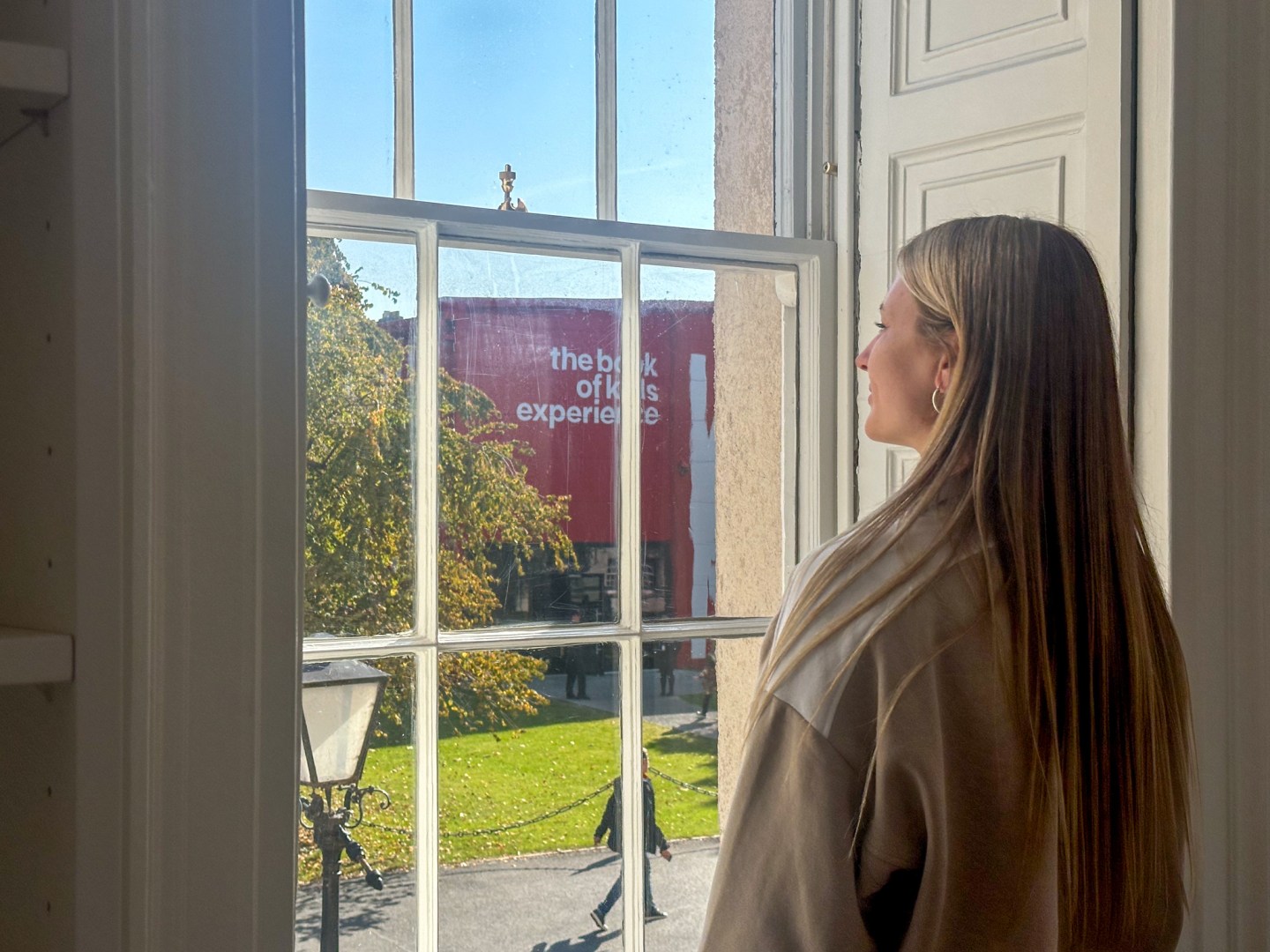 A women looking out the window of Trinity on-campus accommodation, to The Book of Kells Experience Exhibition