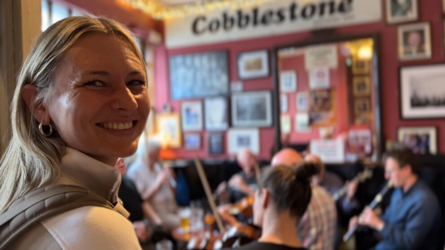 Image of a women smiling while a trad band play music in a pub