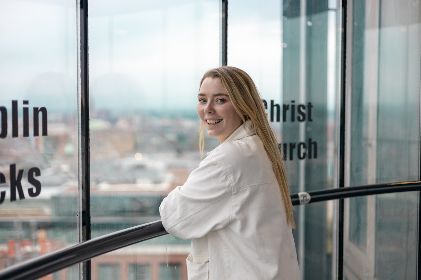A women wearing a white denim jacket smiles as she looks out of Smithfield tower