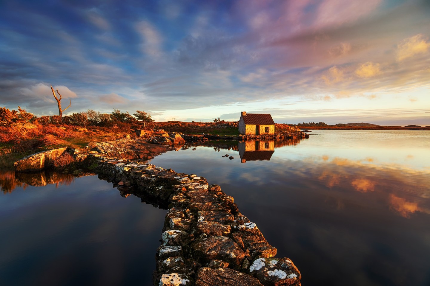 Sunset over water with stoney walls and a traditional white house