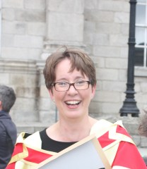 Photo of Dr Jane Maxwell in a red and gold robe on Trinity Campus