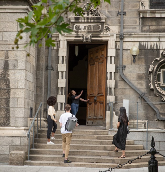 3 people stand at a historic doorway in Trinity with a tour guide