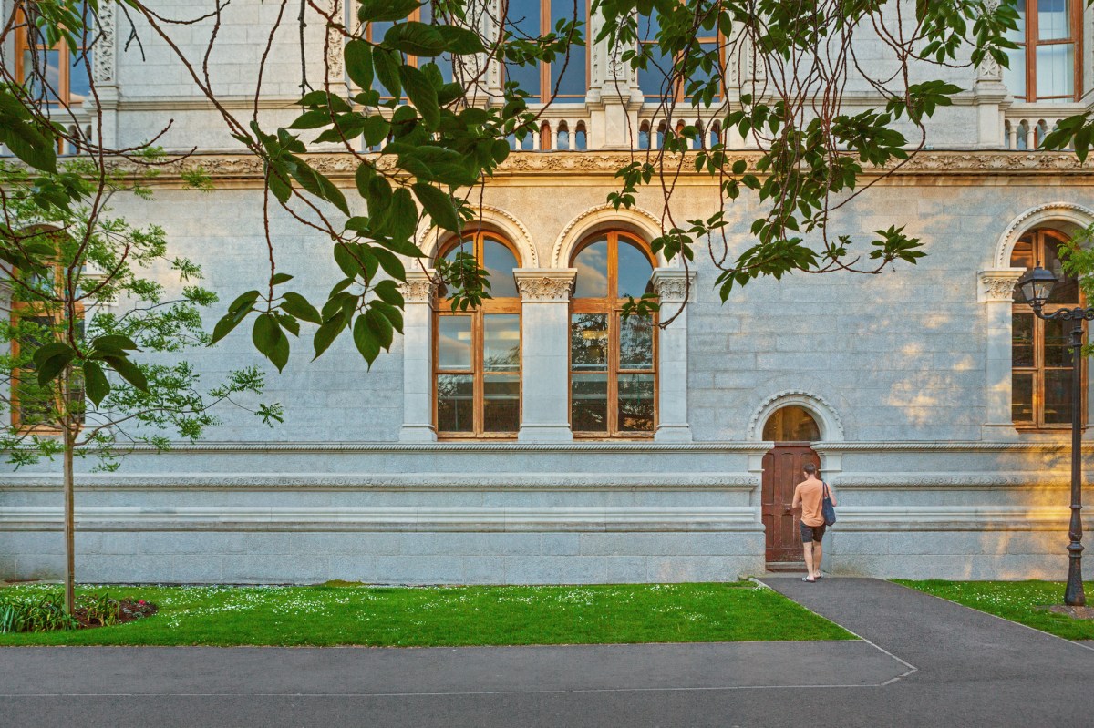 Image of a man with a navy tote bag walking into a building on Trinity campus
