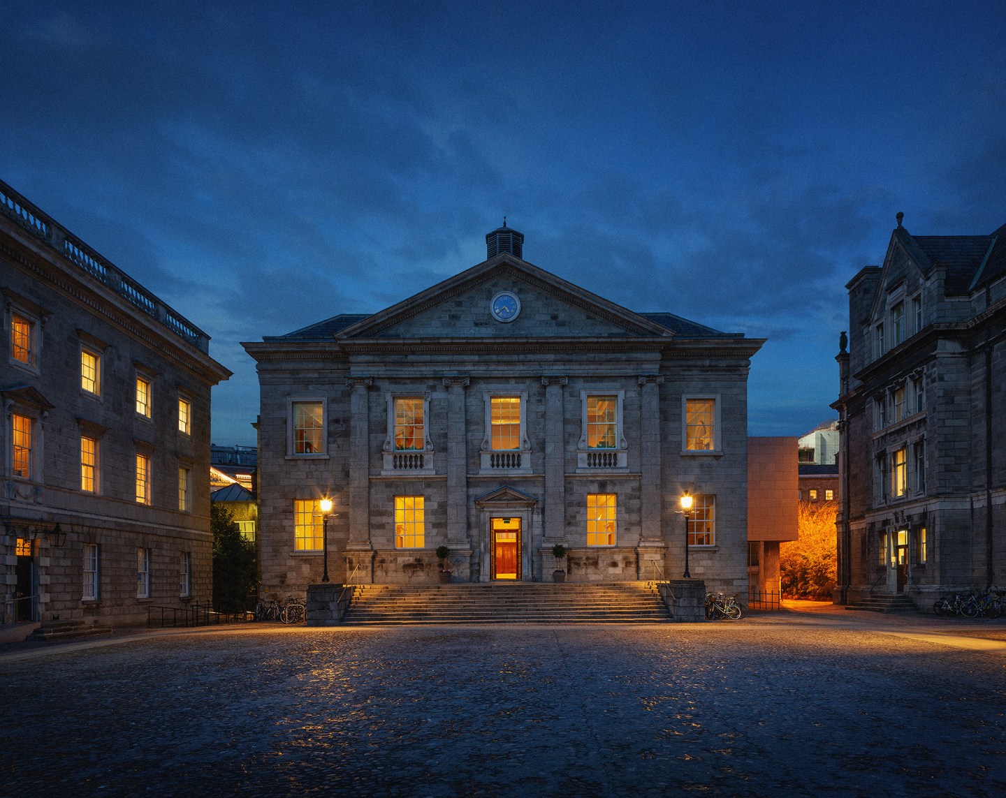 An 18th century building is lit up with yellow lights under a dark blue sky