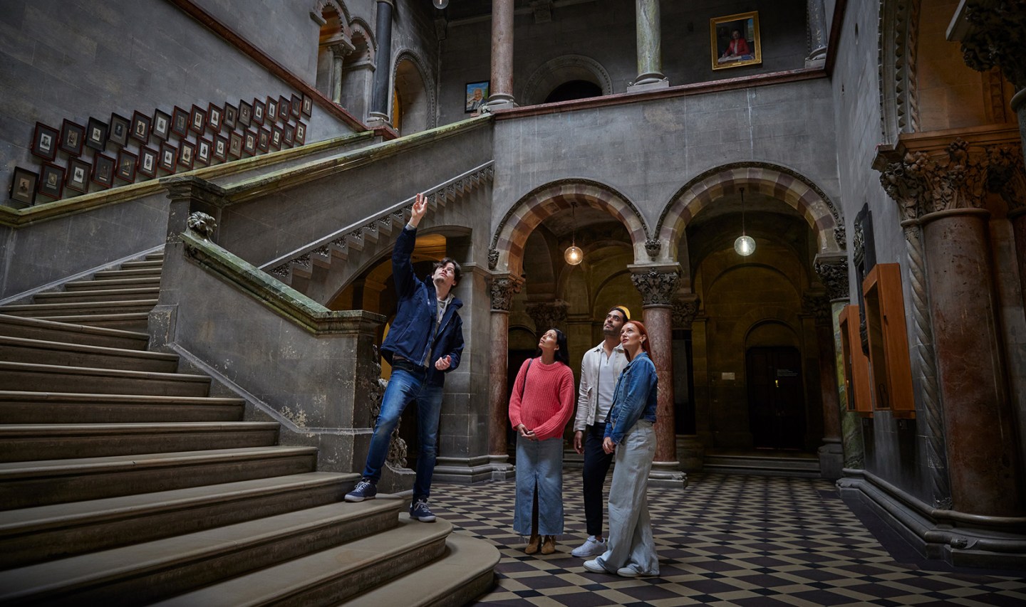 Photo of a tour guide with three tourists admiring the ceiling of the entrance hall