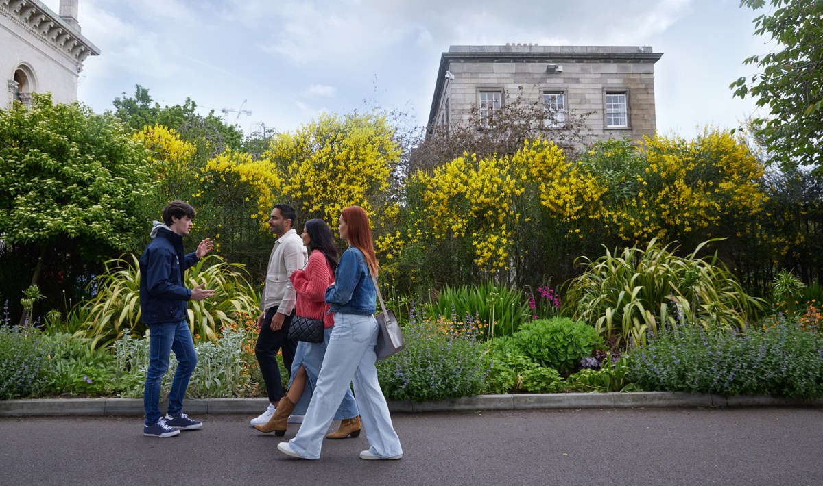 Three tourists and a tour guide walking along a path discussing the rose garden and ecosystem on Trinity campus