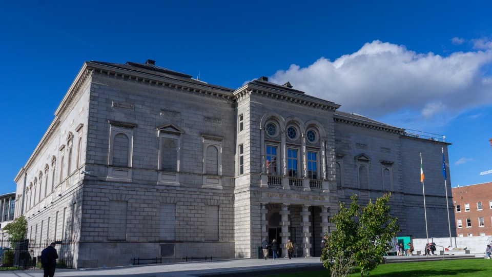 A large grey building featuring numerous windows and columns at the front,.