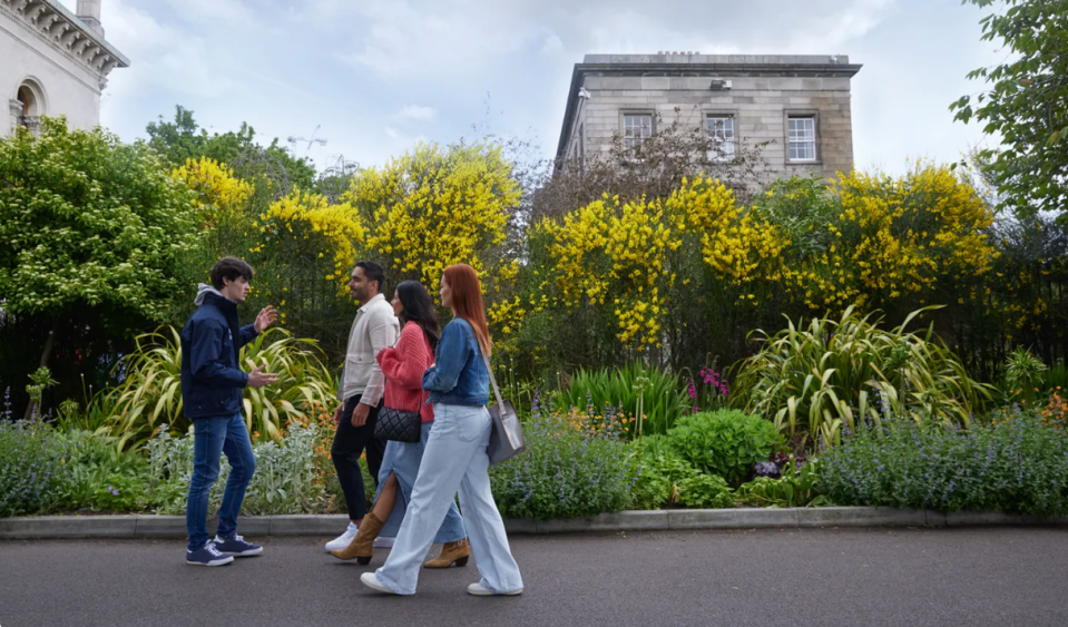 A guide walks near blossoming flowers on Trinity campus with a group of 3 people.